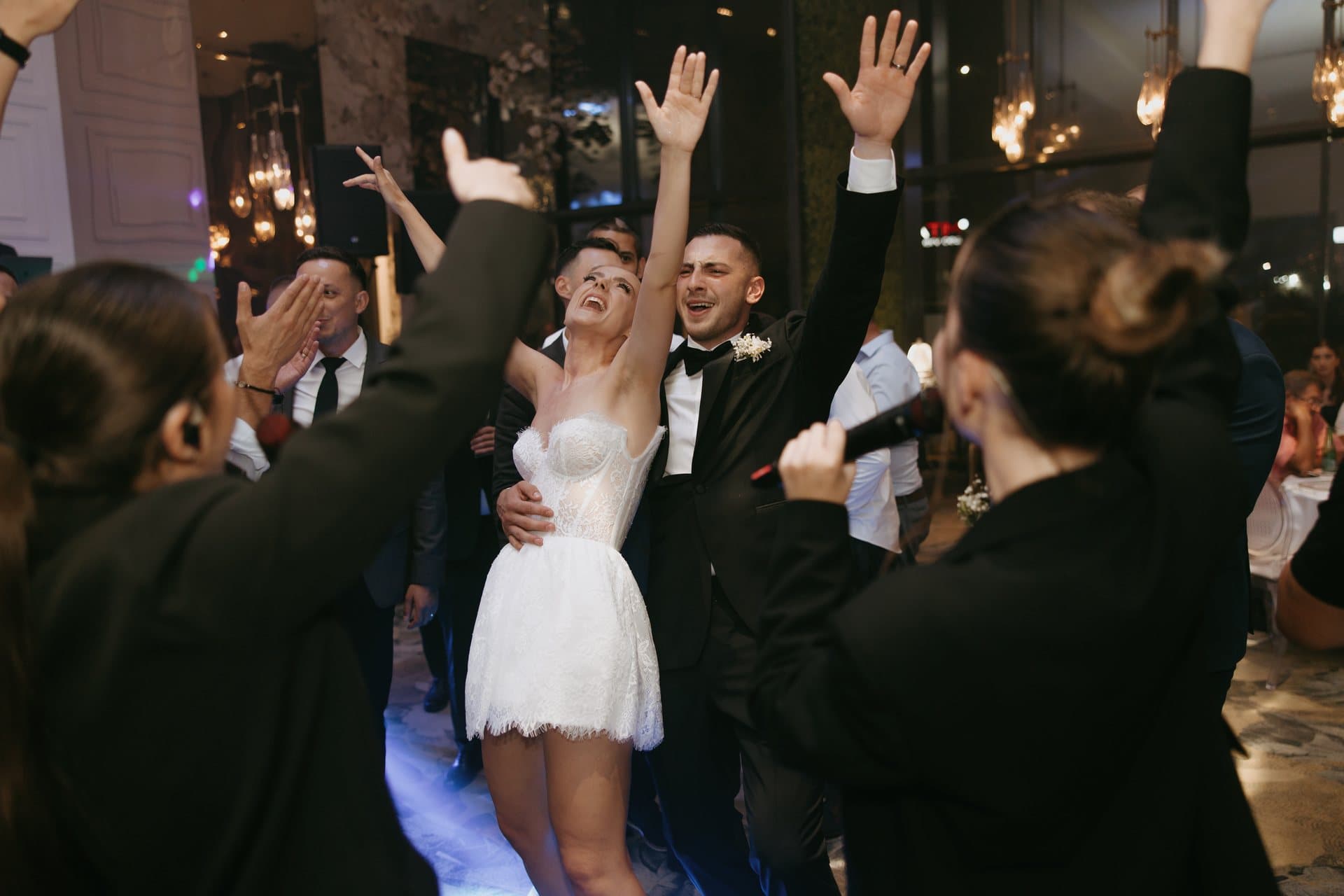 Mireasa dansează cu mâinile ridicate în mijlocul invitaților și al artiștilor