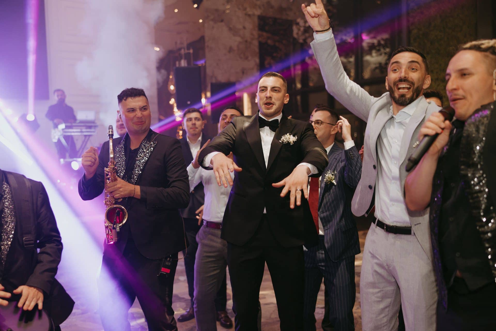 Saxofonistul și solistul cântă printre invitați, care dansează cu mâinile ridicate